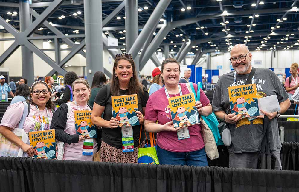 Five attendees, four women and one man holding up books in the Authors Area of TLA Annual Conference.