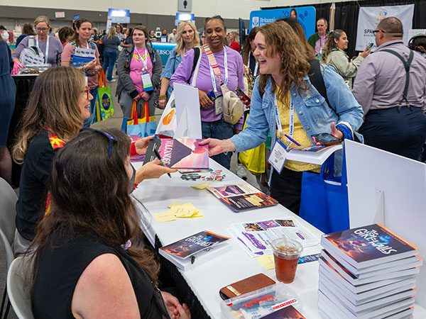 Two author sitting at a table and one hands a book to an attendee in line.
