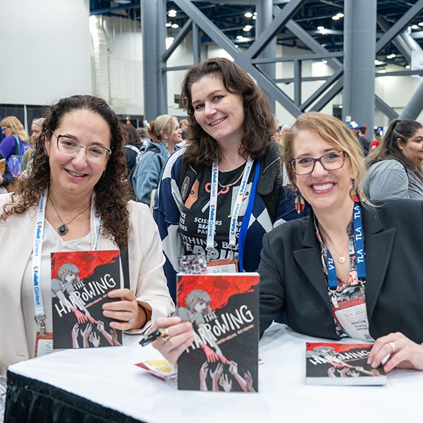 Two female attendees and a female author in the TLA Authors Area in the Annual Conference exhibit hall.