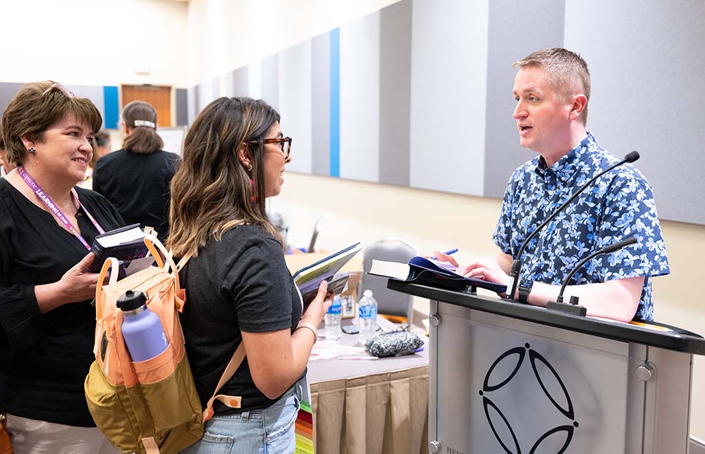 Male speaker at a podium talking with two women