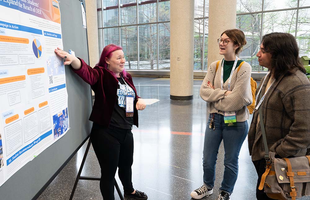 A woman presenting a poster session in front of a board at TLA's Annual Conference to two female attendees.
