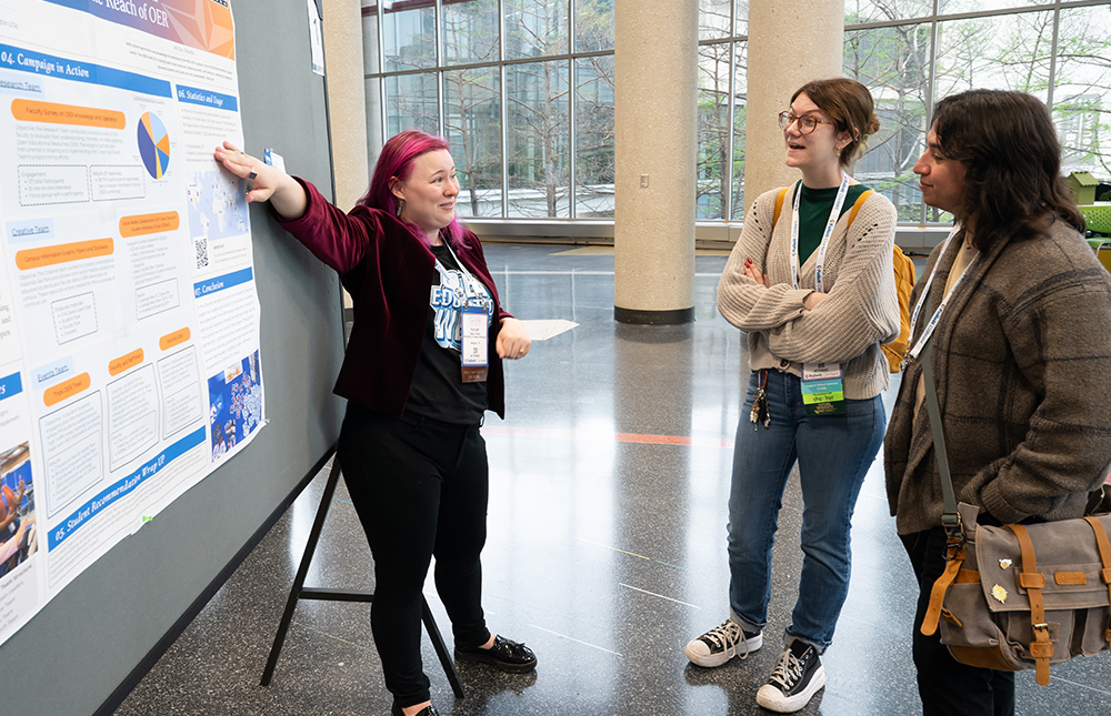 A woman presenting a poster session in front of a board at TLA's Annual Conference to two female attendees.
