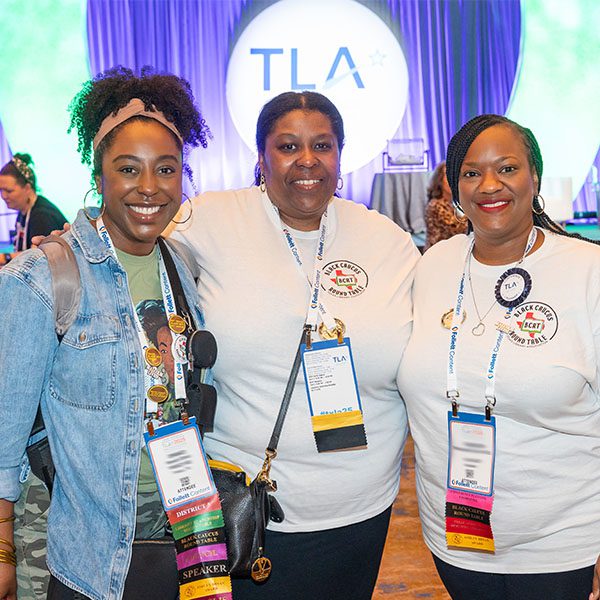 Three women attendees of TLA Annual Conference in front of the keynote stage and TLA sign
