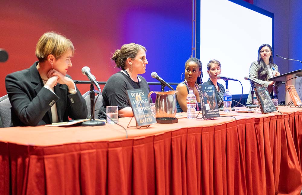 Four authors sitting at a table speaking with a moderator at a podium.
