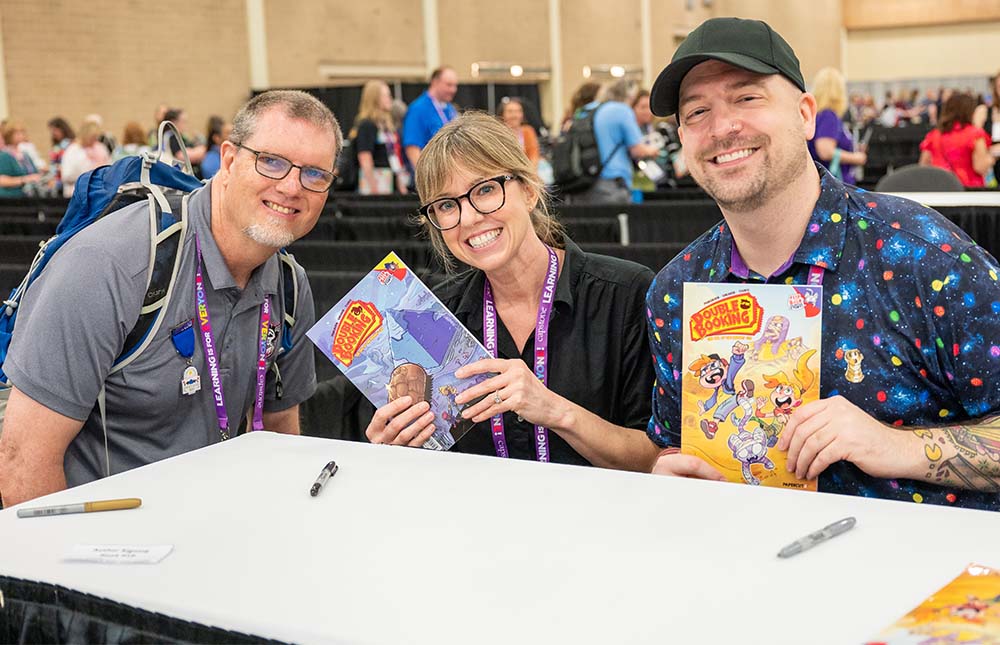 Attendee getting books signed by two authors at TLA Annual Conference Authors Area