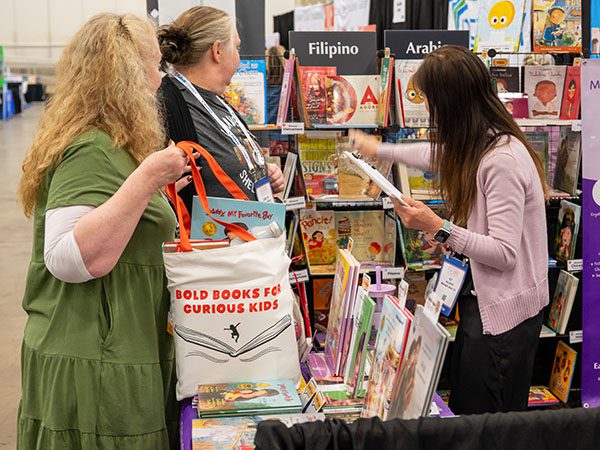 Three women looking at books at a booth in the exhibit hall.