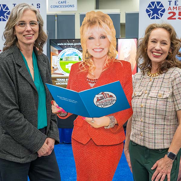 TLA President and Executive Director in the exhibit hall with cutout of Dolly Parton with a book